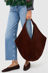 Person showcasing classic, high-end Chocolate Soft M Hobo tote in brown suede, paired with light-wash jeans and suede flats, exuding effortless, fun style.