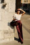 Woman in cream top and burgundy trousers showcases an Oxblood Croc-Embossed Waist Belt, embodying effortless, classic style with a high-end, fun touch.
