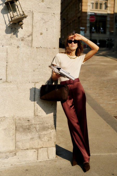 Woman in cream top and burgundy trousers showcases an Oxblood Croc-Embossed Waist Belt, embodying effortless, classic style with a high-end, fun touch.