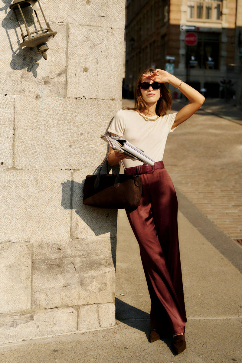 Woman in cream top and burgundy trousers showcases an Oxblood Croc-Embossed Waist Belt, embodying effortless, classic style with a high-end, fun touch.