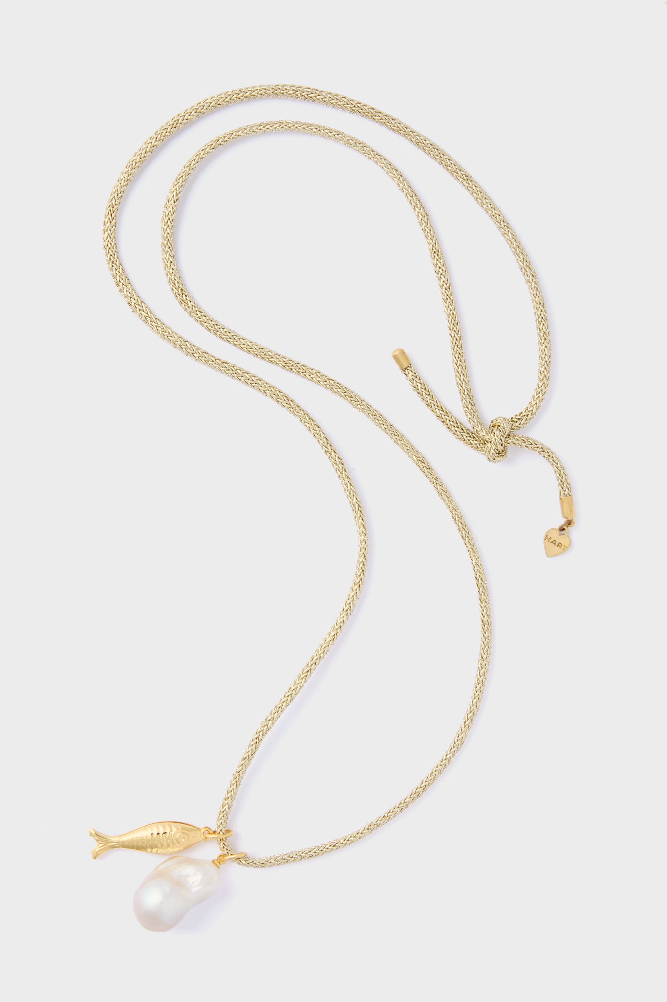 The HART Gold Lurex Cord Necklace features a gold fish charm and an eye-catching baroque pearl pendant, adding a touch of elegance to any outfit.