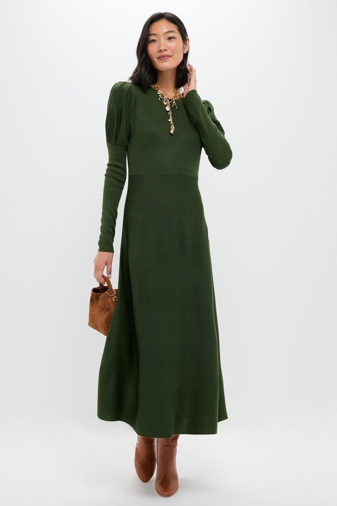 A woman in a Pomander Place fit-and-flare maxi sweater dress with puffed shoulders, brown boots, a statement necklace, and a small brown handbag stands against a plain background.