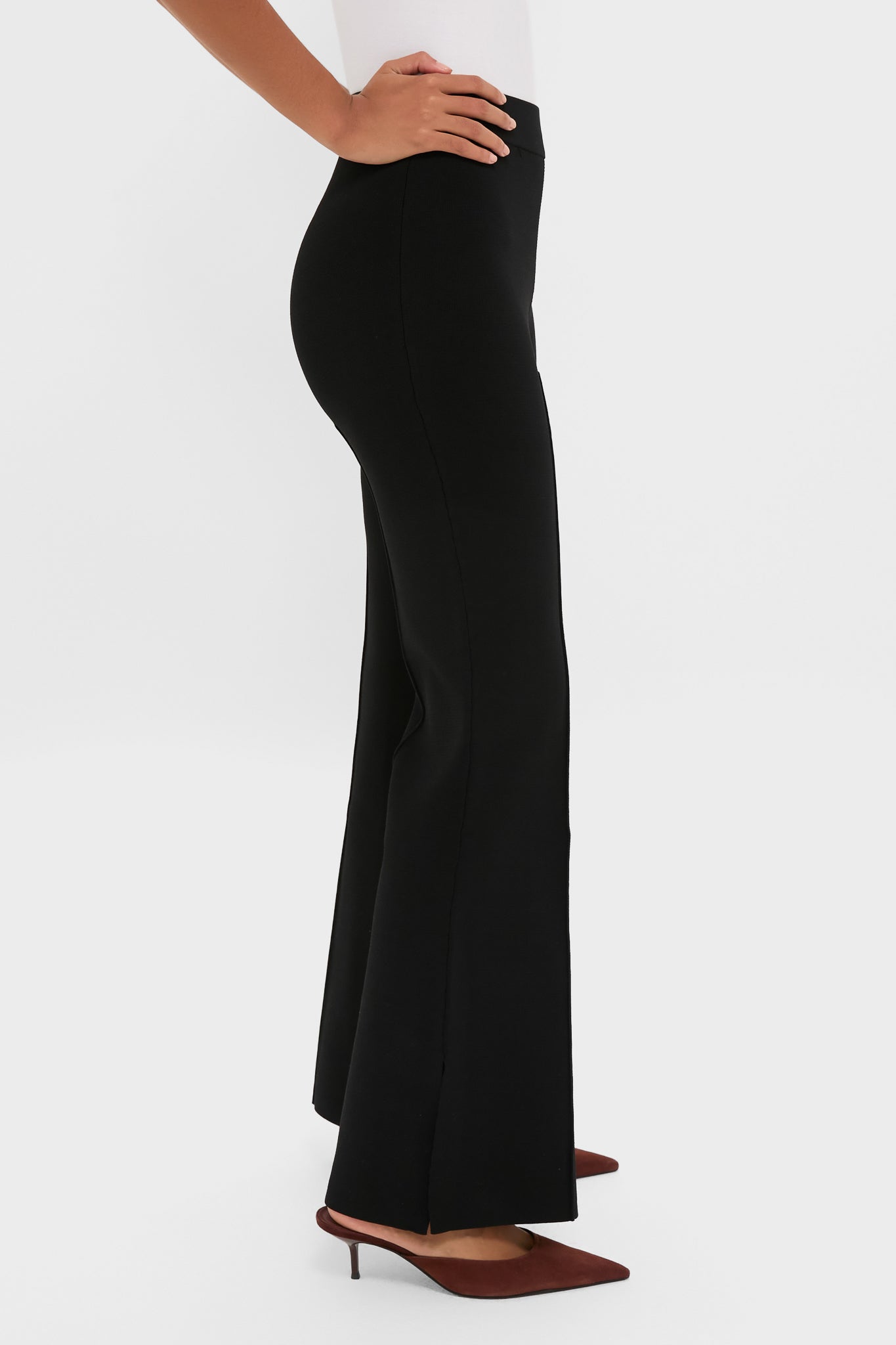 Side view of Black Hana Pull On Full Flare trousers, high-waisted with a slight flare and front slit, worn with reddish-brown mules, exuding classic, effortless sophistication.