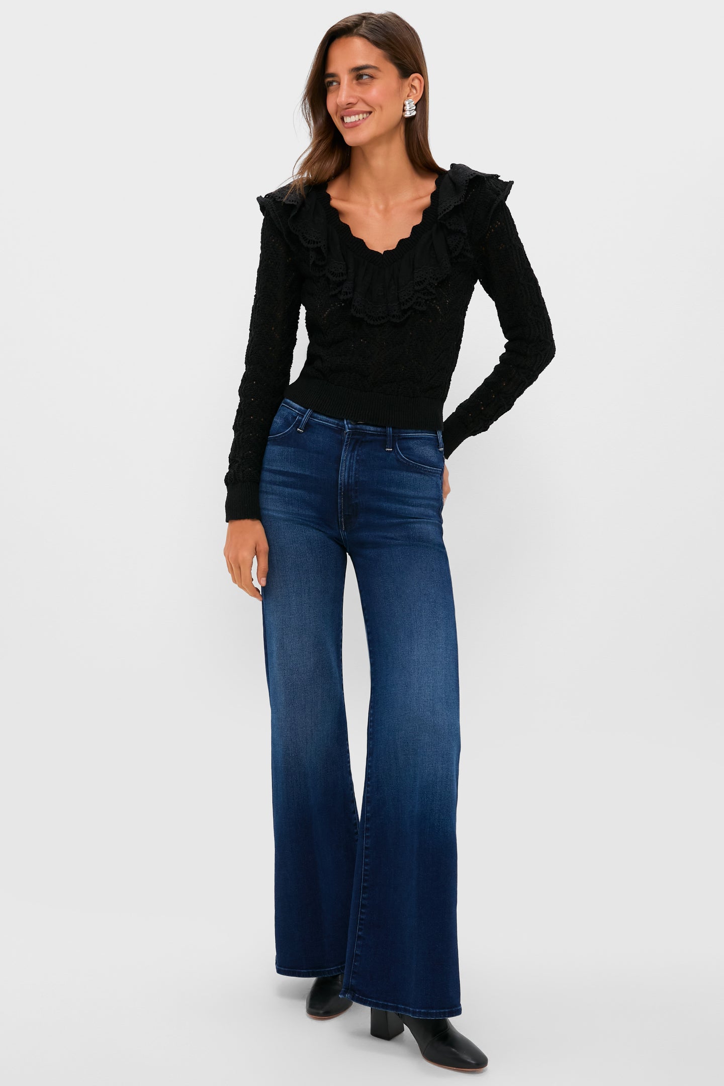 Model wears Black Pointelle Knit Sherry Top with ruffled V-neck and embroidered trim, paired with wide-leg jeans and block-heel boots, embodying effortless, high-end style.