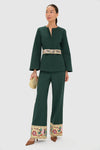 A woman wears a Tuckernuck dark green pantsuit with balloon sleeves, a jacquard floral embroidered belt, matching pant hems, styled with a beige clutch and brown pointed shoes.