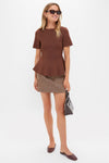 Model in Chocolate Brown Knit Phoebe Peplum Top, classic and effortless, paired with a high-waisted skirt, embodying fun and high-end style with tortoiseshell sunglasses and a structured handbag.