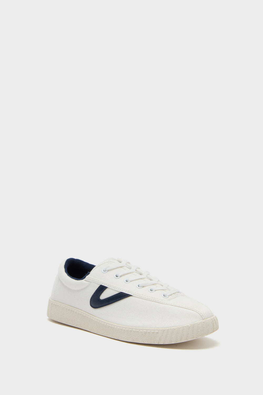 The Tretorn low-top white canvas sneaker features a navy blue V logo on the side, white laces, and a beige rubber sole, drawing inspiration from luxury sports shoe design.