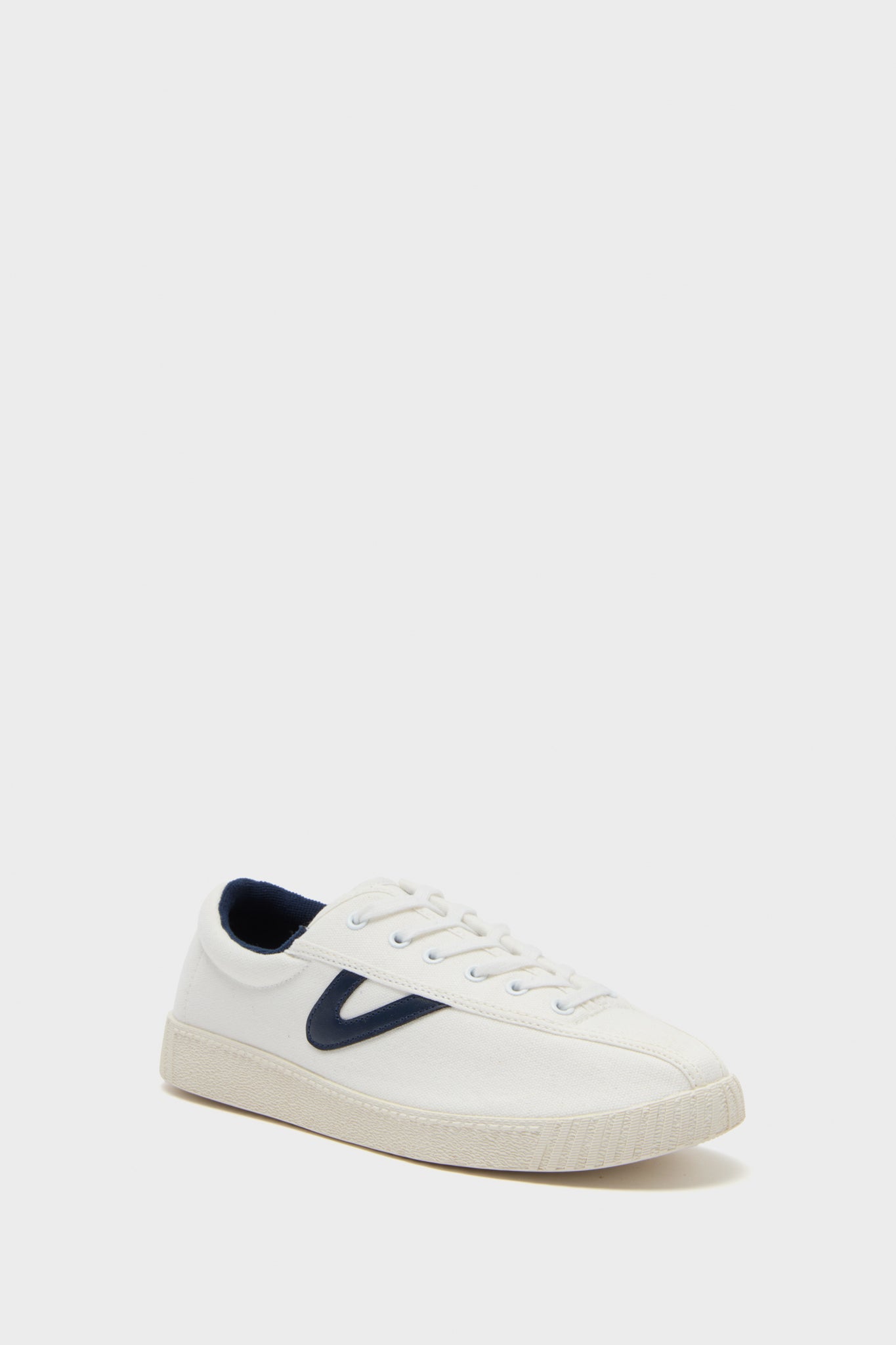 The Tretorn low-top white canvas sneaker features a navy blue V logo on the side, white laces, and a beige rubber sole, drawing inspiration from luxury sports shoe design.