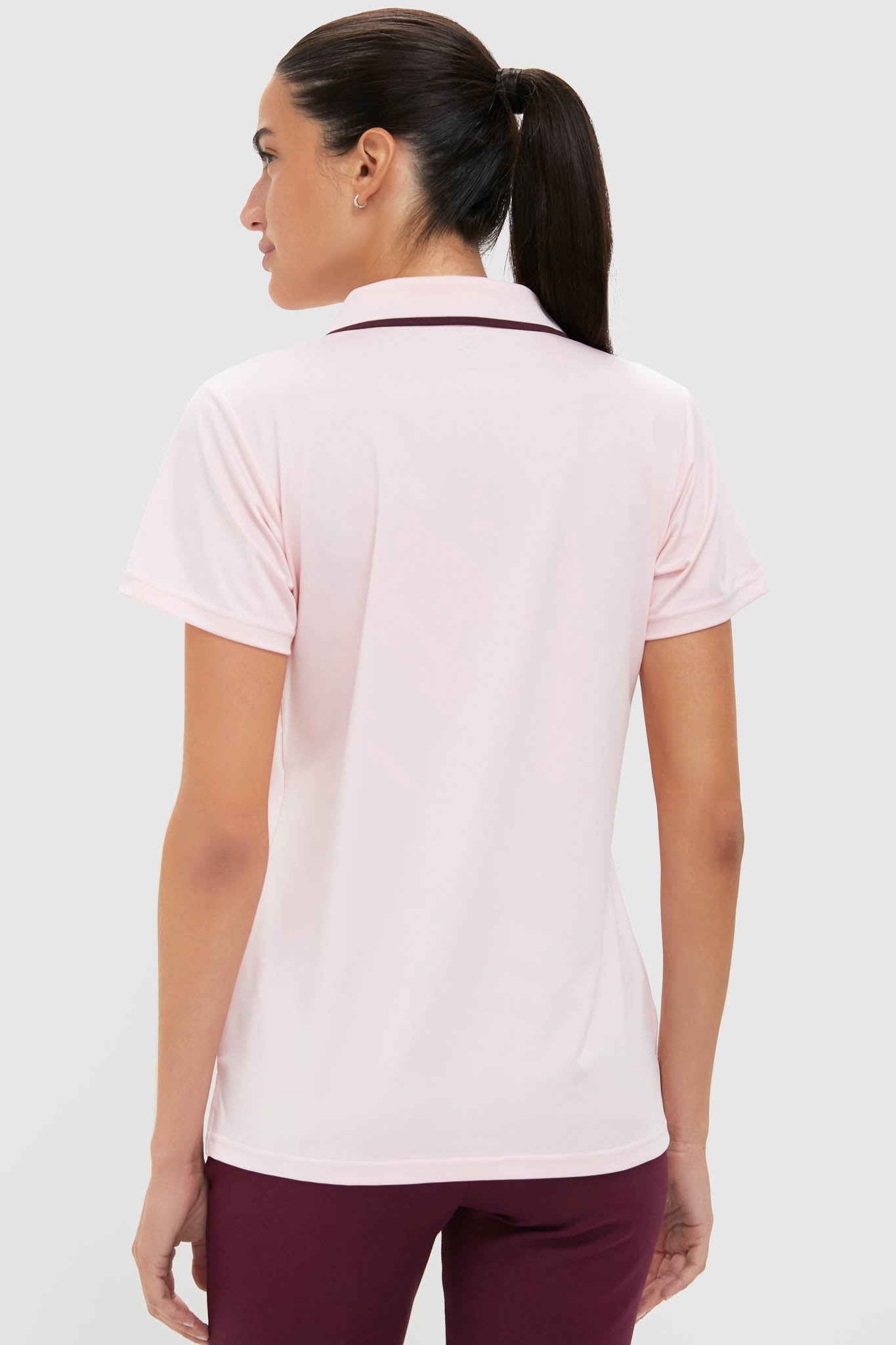 Woman in a light-pink Caroline Polo, showcasing a classic, effortless style with a fitted silhouette and rib trim collar, paired with dark burgundy pants.