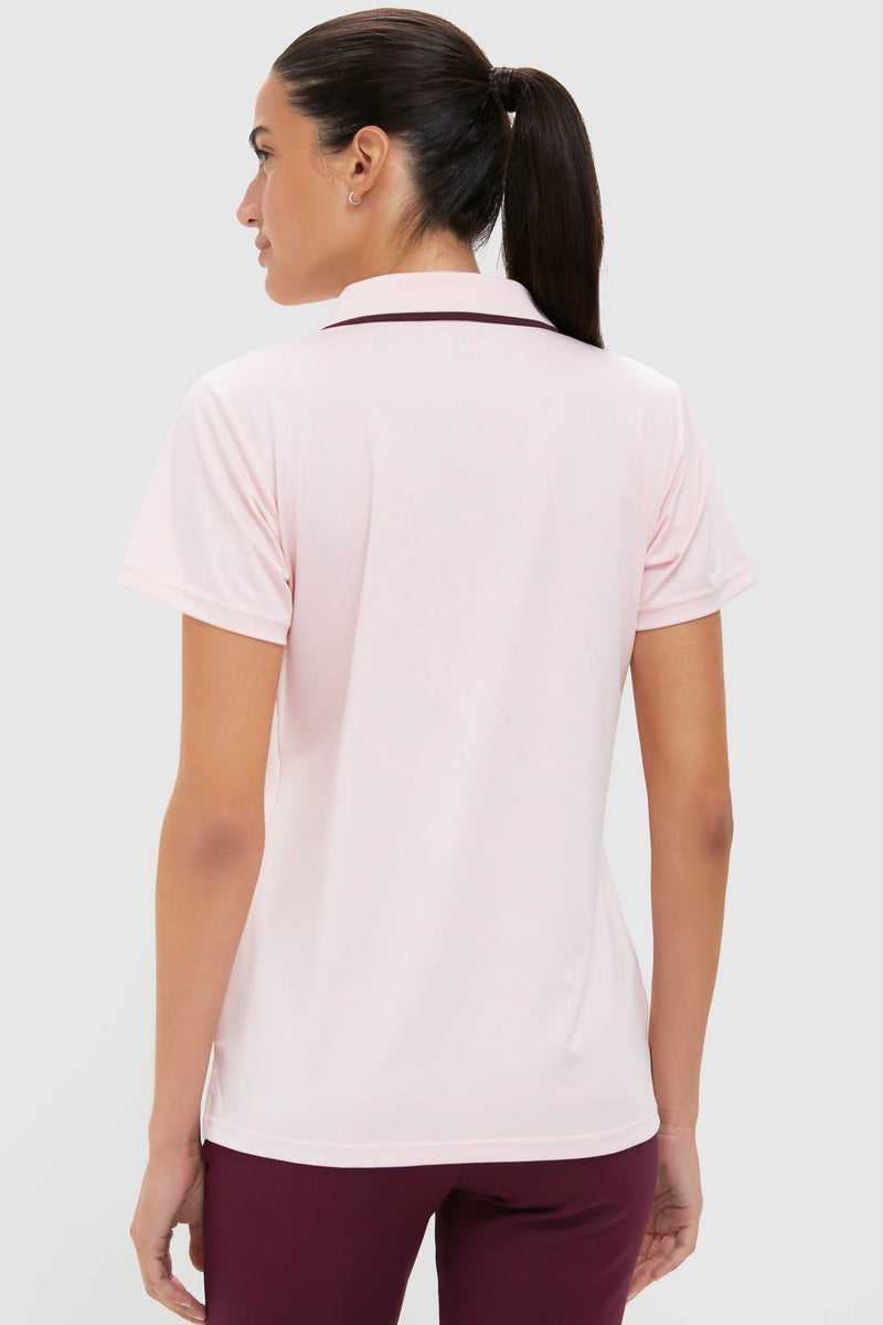 Woman in a light-pink Caroline Polo, showcasing a classic, effortless style with a fitted silhouette and rib trim collar, paired with dark burgundy pants.