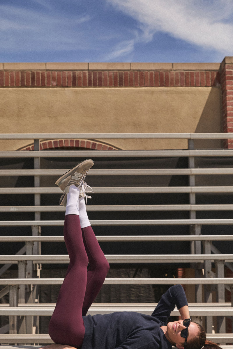 Person reclining on bleachers, showcasing classic Winetasting High Rise Long Compression Spandex MacKenzie Legging, effortlessly combining fun style and high-end comfort with a flattering fit.