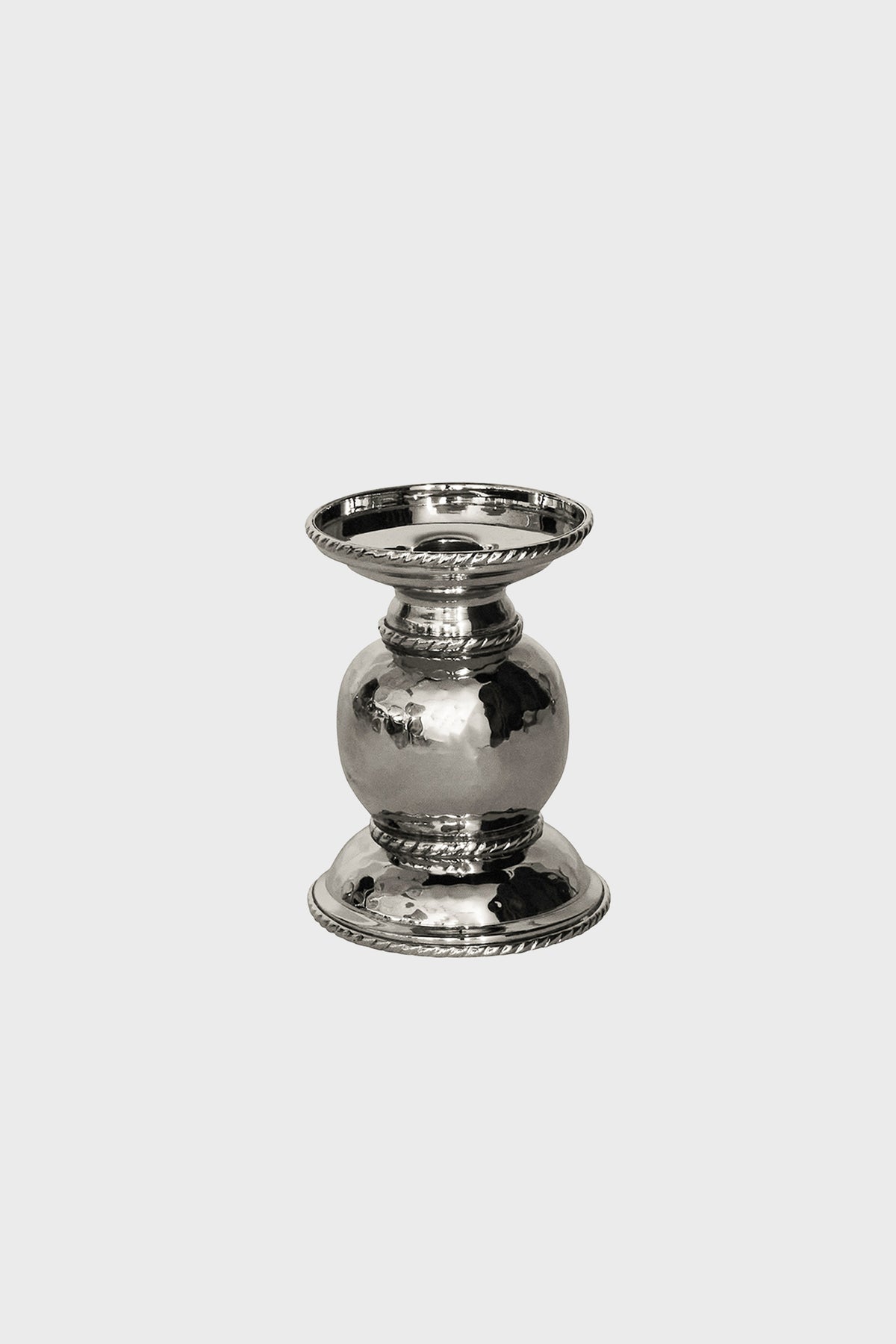 A small, polished silver candle holder with a rounded center, flat base, and decorative ridged edges—crafted in hammered stainless steel by Juliska for an elegant touch.