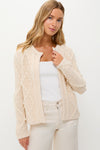 A woman wears a Hyacinth House cable knit cardigan with textured patterns over a white top and cream pants, creating a chic winter white sweater look.