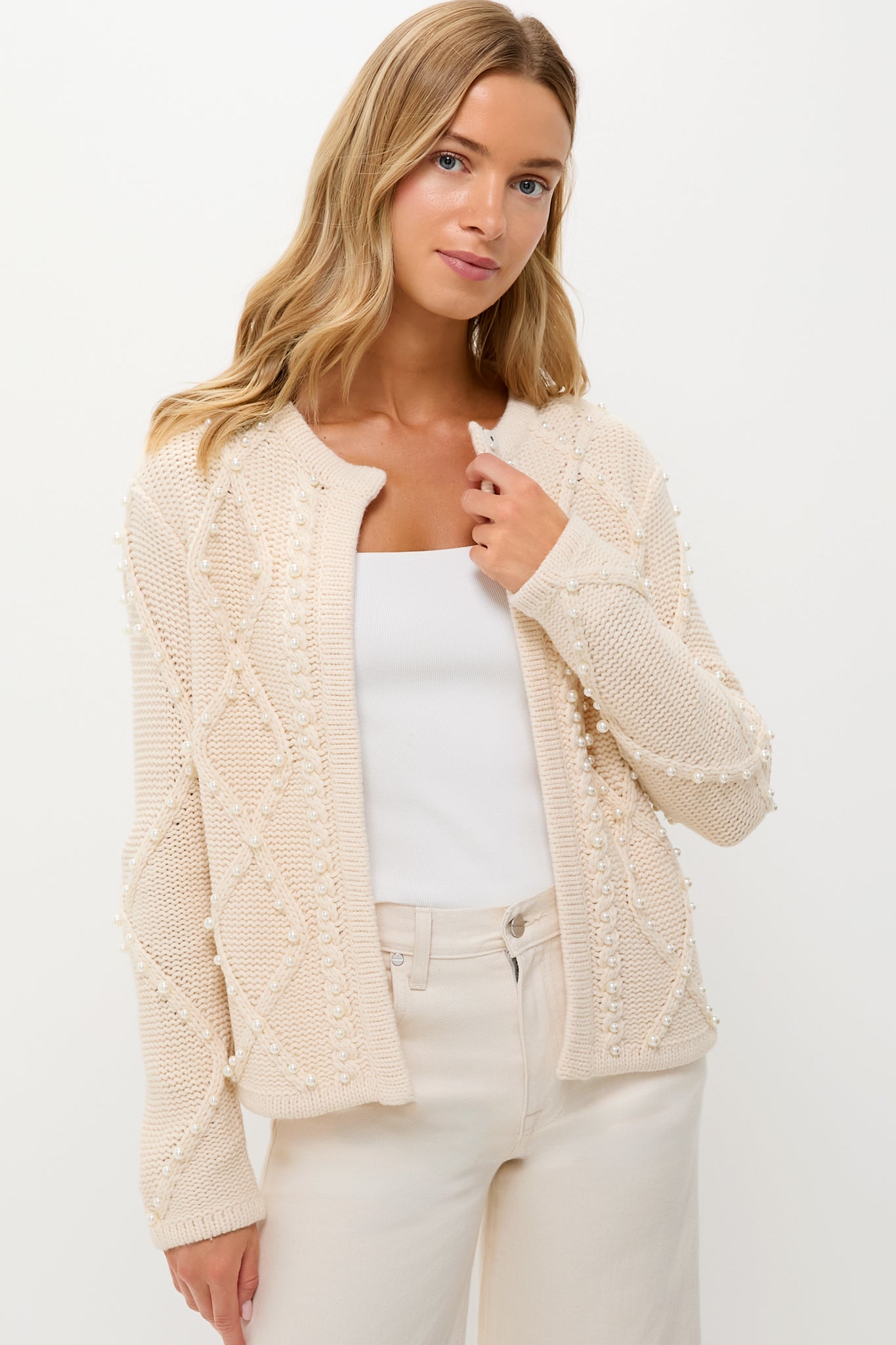A woman wears a Hyacinth House cable knit cardigan with textured patterns over a white top and cream pants, creating a chic winter white sweater look.