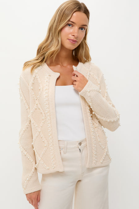 A woman wears a Hyacinth House cable knit cardigan with textured patterns over a white top and cream pants, creating a chic winter white sweater look.