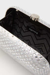 Close-up of an open Olga Berg evening bag with a silver textured, reflective exterior and black zigzag-patterned fabric lining with the Olga Berg label inside.