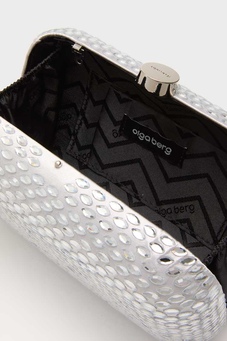 Close-up of an open Olga Berg evening bag with a silver textured, reflective exterior and black zigzag-patterned fabric lining with the Olga Berg label inside.