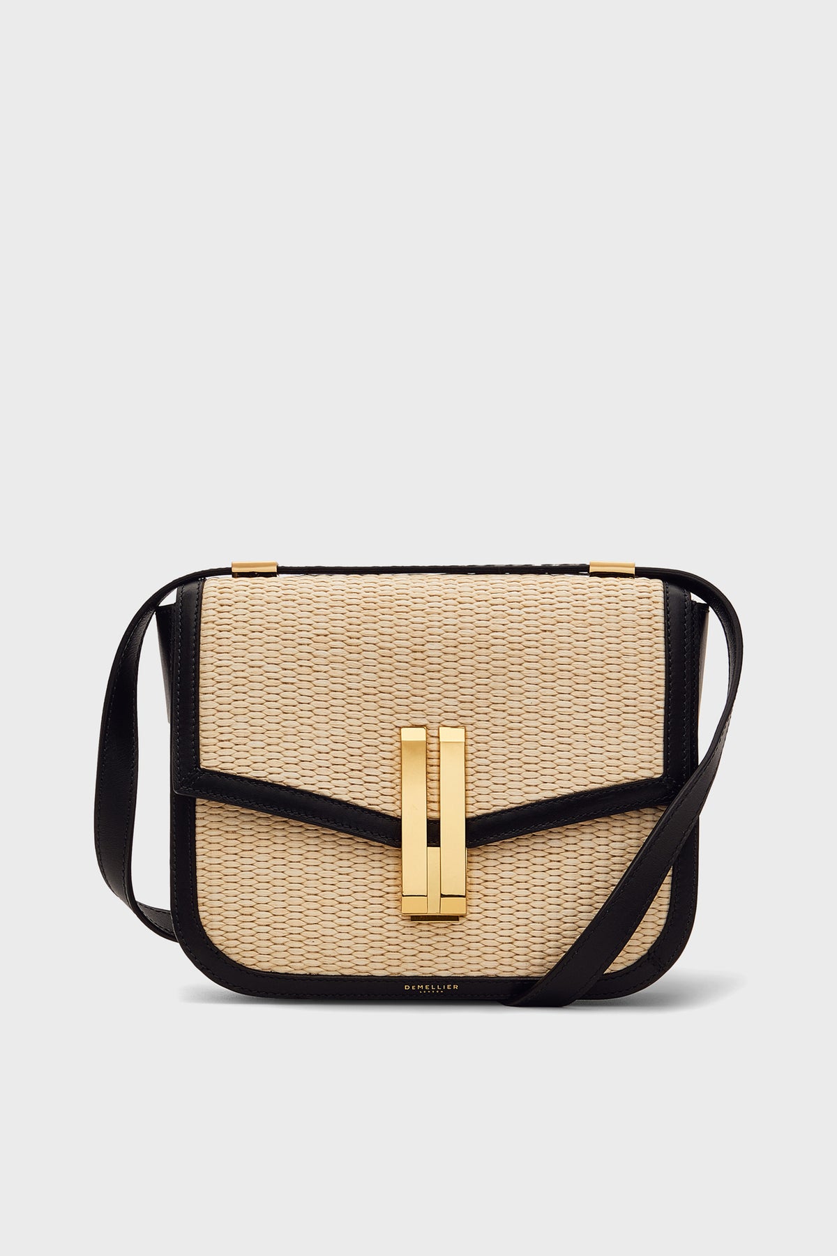 A close-up of a Demellier natural raffia bag with an adjustable crossbody strap, highlighting the beauty of handcrafted handbags.