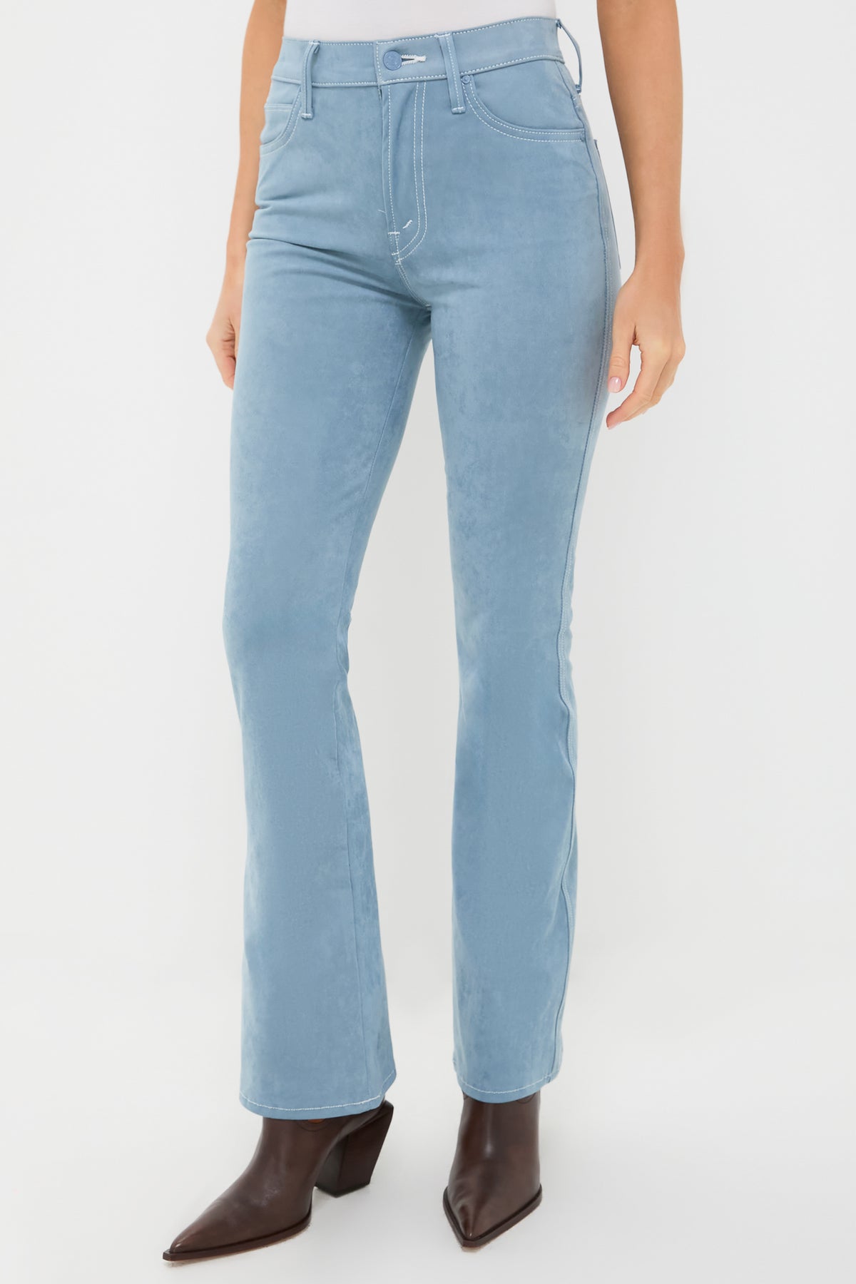 A person wears high rise flare pants from MOTHER in light blue, paired with brown pointed-toe heeled boots.