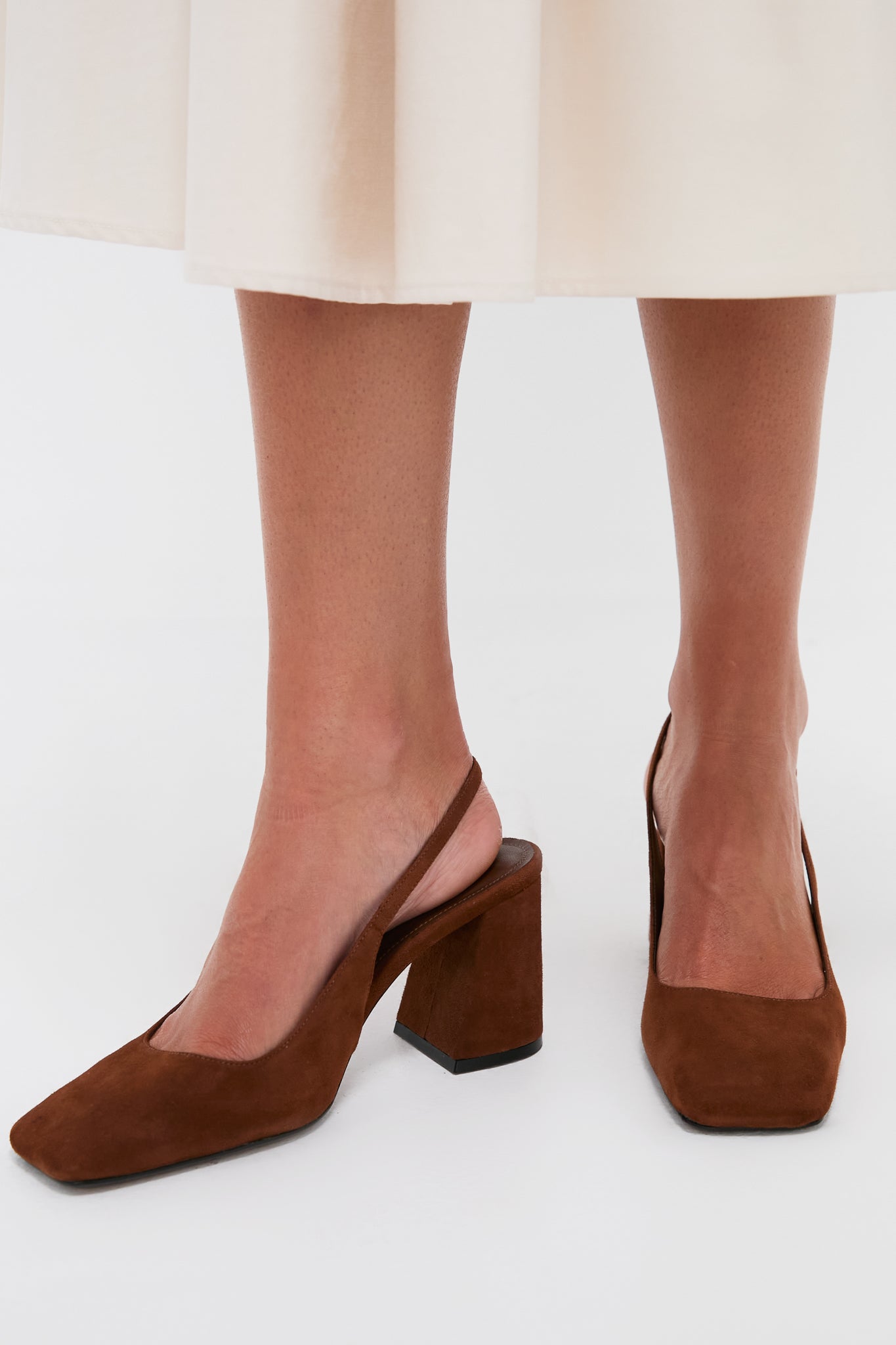 Model wearing Pecan Brown Leia Block Sling Back Heels, showcasing their classic suede design and square toe, paired effortlessly with a cream midi skirt for a high-end, fun look.