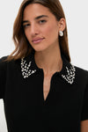 A woman models a Tuckernuck black knit polo with an embellished collar and silver hoop earrings against a plain background.
