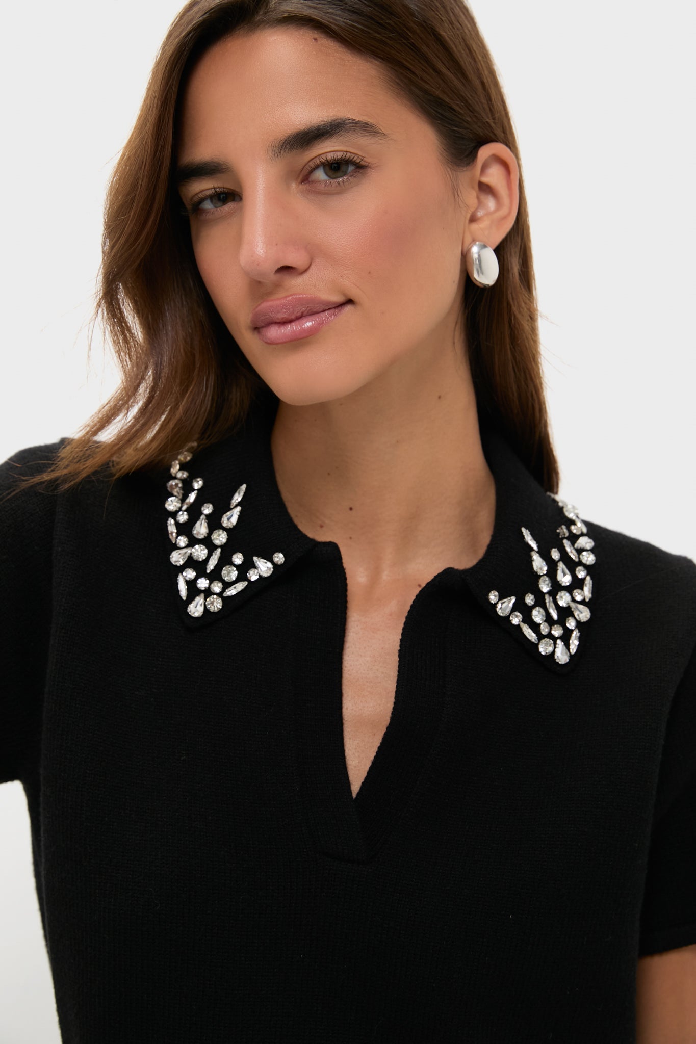 A woman models a Tuckernuck black knit polo with an embellished collar and silver hoop earrings against a plain background.