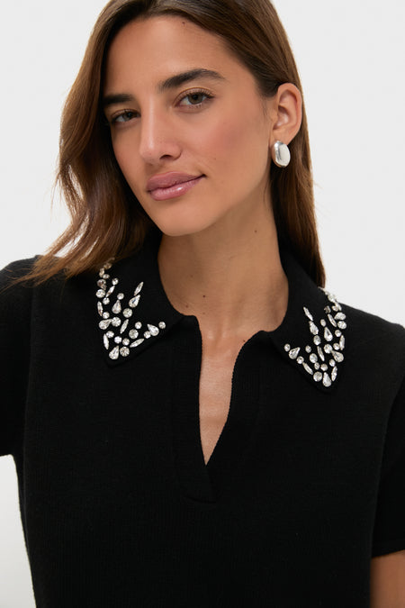 A woman models a Tuckernuck black knit polo with an embellished collar and silver hoop earrings against a plain background.