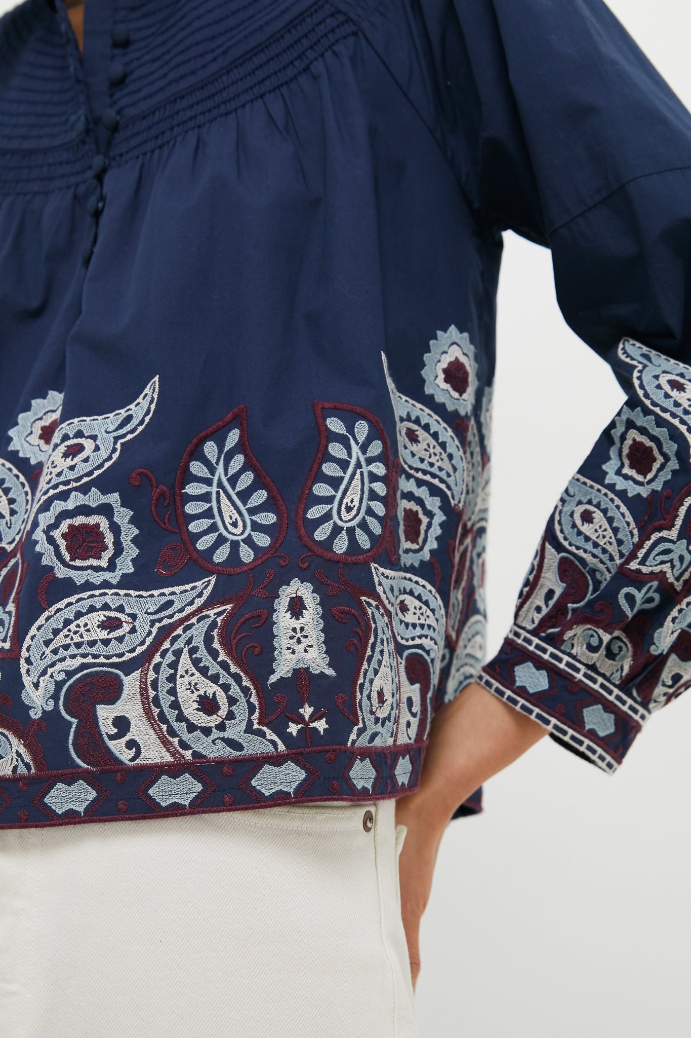 Navy Embroidered Lucia Blouse with classic puff sleeves and intricate embroidery, styled effortlessly with light bottoms, exudes fun and high-end fashion.
