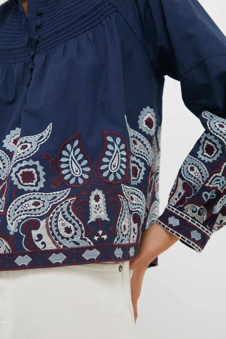 Navy Embroidered Lucia Blouse with classic puff sleeves and intricate embroidery, styled effortlessly with light bottoms, exudes fun and high-end fashion.