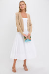 A woman wearing a Pomander Place relaxed fit beige cardigan with tonal buttons over a white midi dress holds a book and stands against a plain white background.