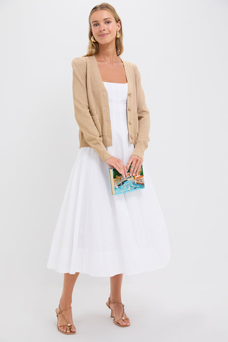 A woman wearing a Pomander Place relaxed fit beige cardigan with tonal buttons over a white midi dress holds a book and stands against a plain white background.