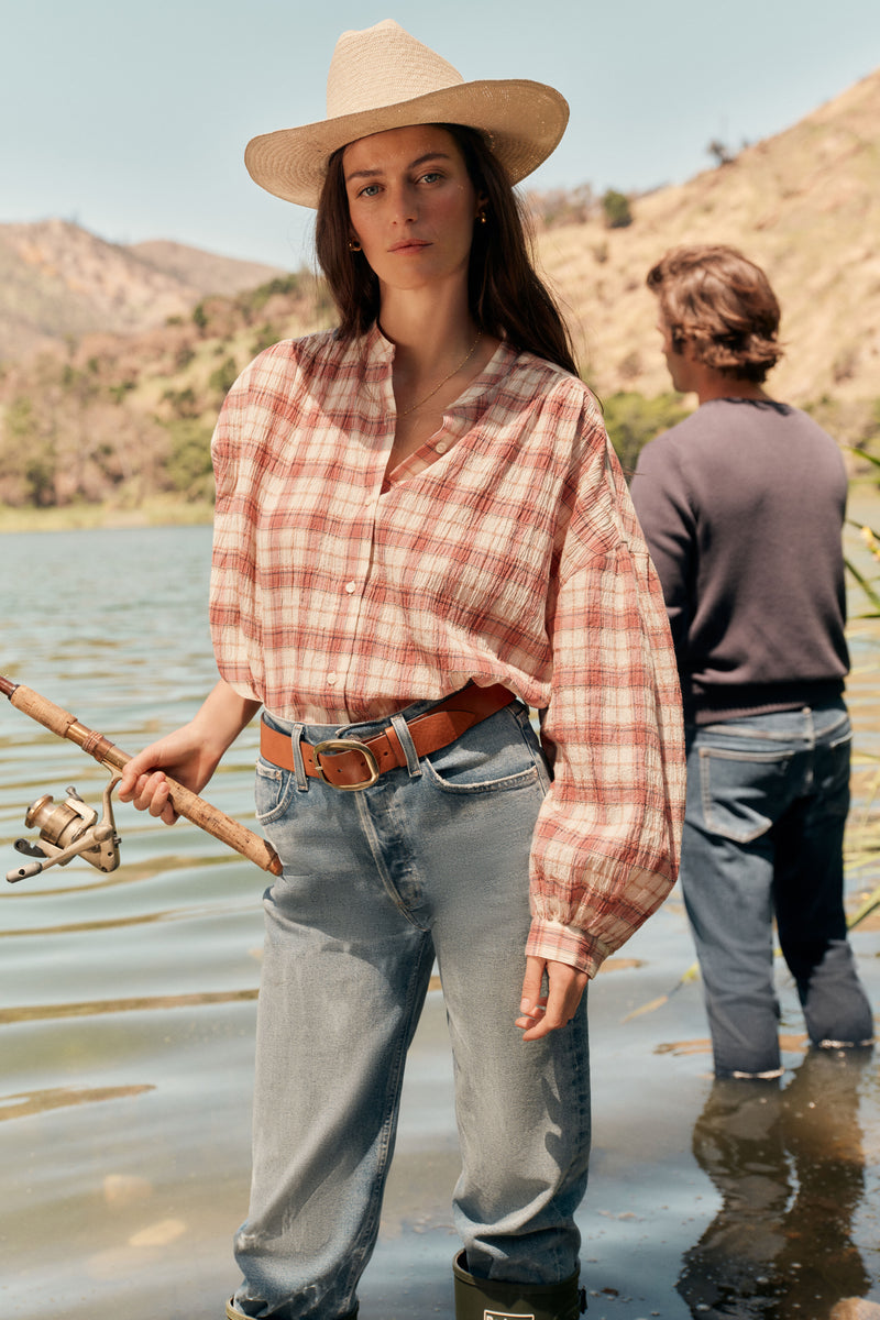 Woman fishing in a lake in a straw hat, plaid shirt, and jeans. 
