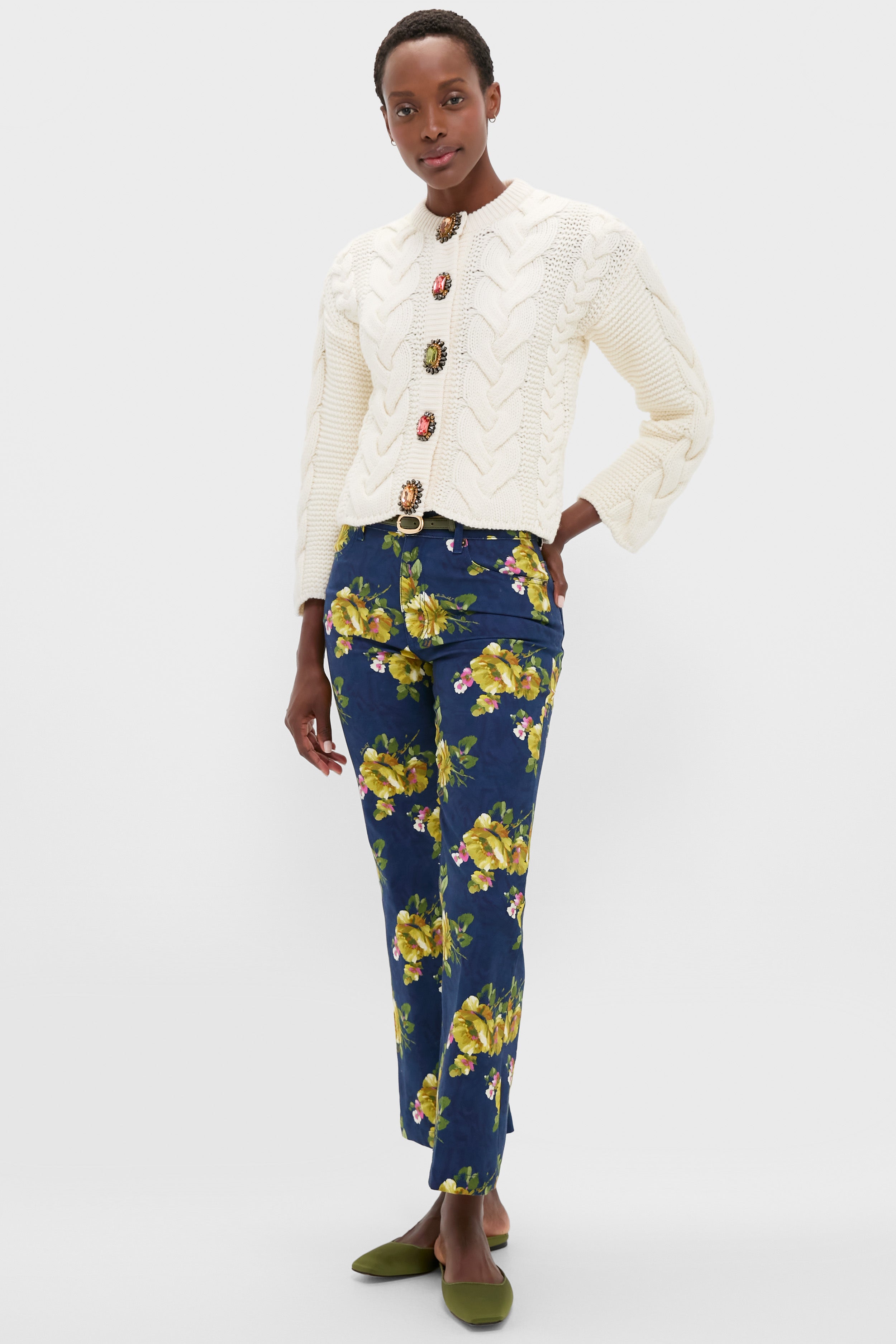 A person wears a La DoubleJ white knit sweater with decorative buttons, blue high waist floral pattern jeans, and green shoes, standing against a plain background.
