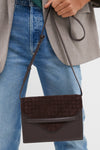 Brown Leather Stevie Crossbody held by a person in blue jeans and gray blazer, featuring a classic woven suede flap, offering an effortless, high-end style for fun, on-the-go days.