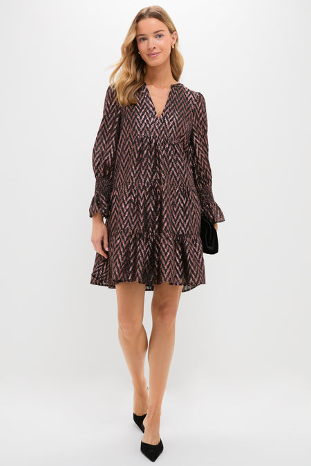 A woman in a loose, patterned Metallic Ikat V-neck dress by Pomander Place, paired with black heels and a black clutch, stands against a plain white background.