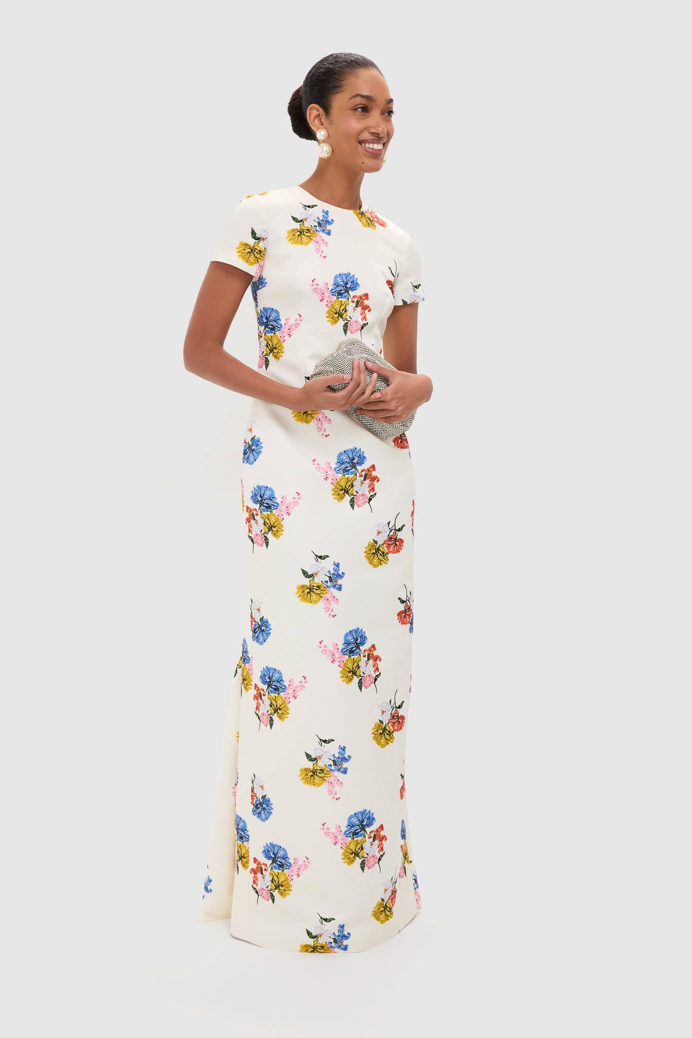 Woman in classic Retro Bouquet on White Fosette Gown with floral pattern, styled with pearl earrings and clutch, embodying an effortless, fun, high-end look.