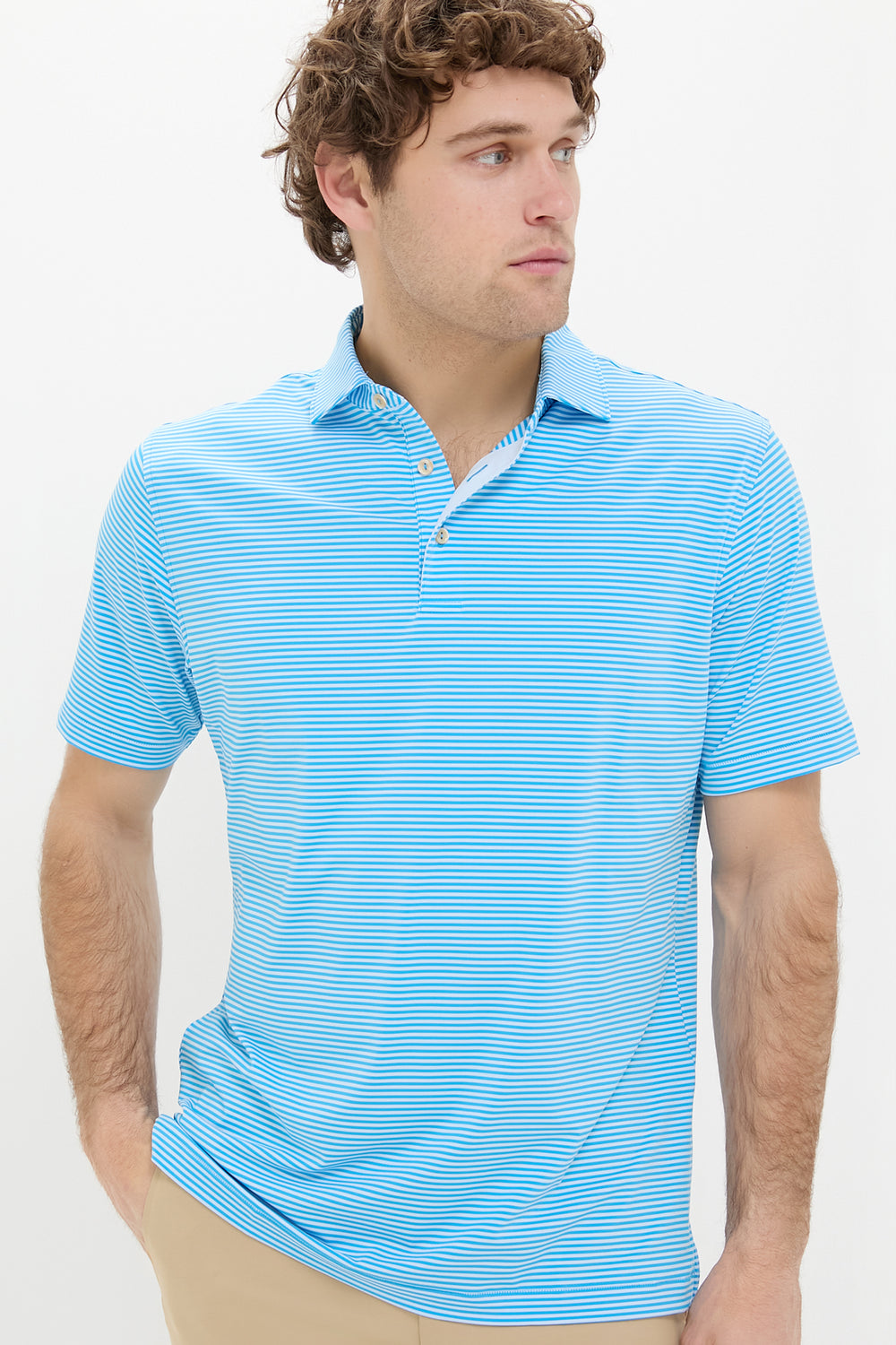 A man confidently wears a Peter Millar light blue and white striped performance jersey polo with four-way stretch, paired with tan pants.