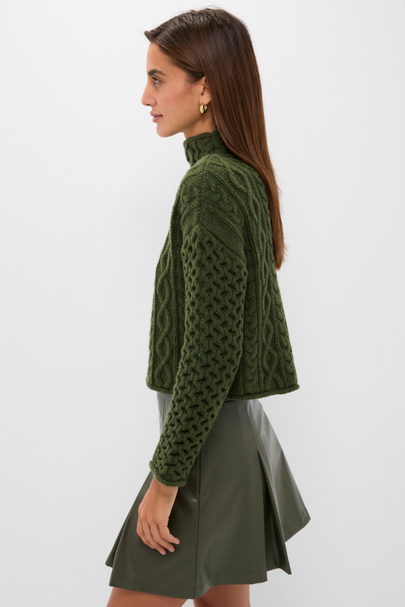 Young woman in a classic, effortless Olive Cable Knit Cropped Perry Turtleneck, paired with a matching faux-leather mini skirt, exuding fun and high-end style.