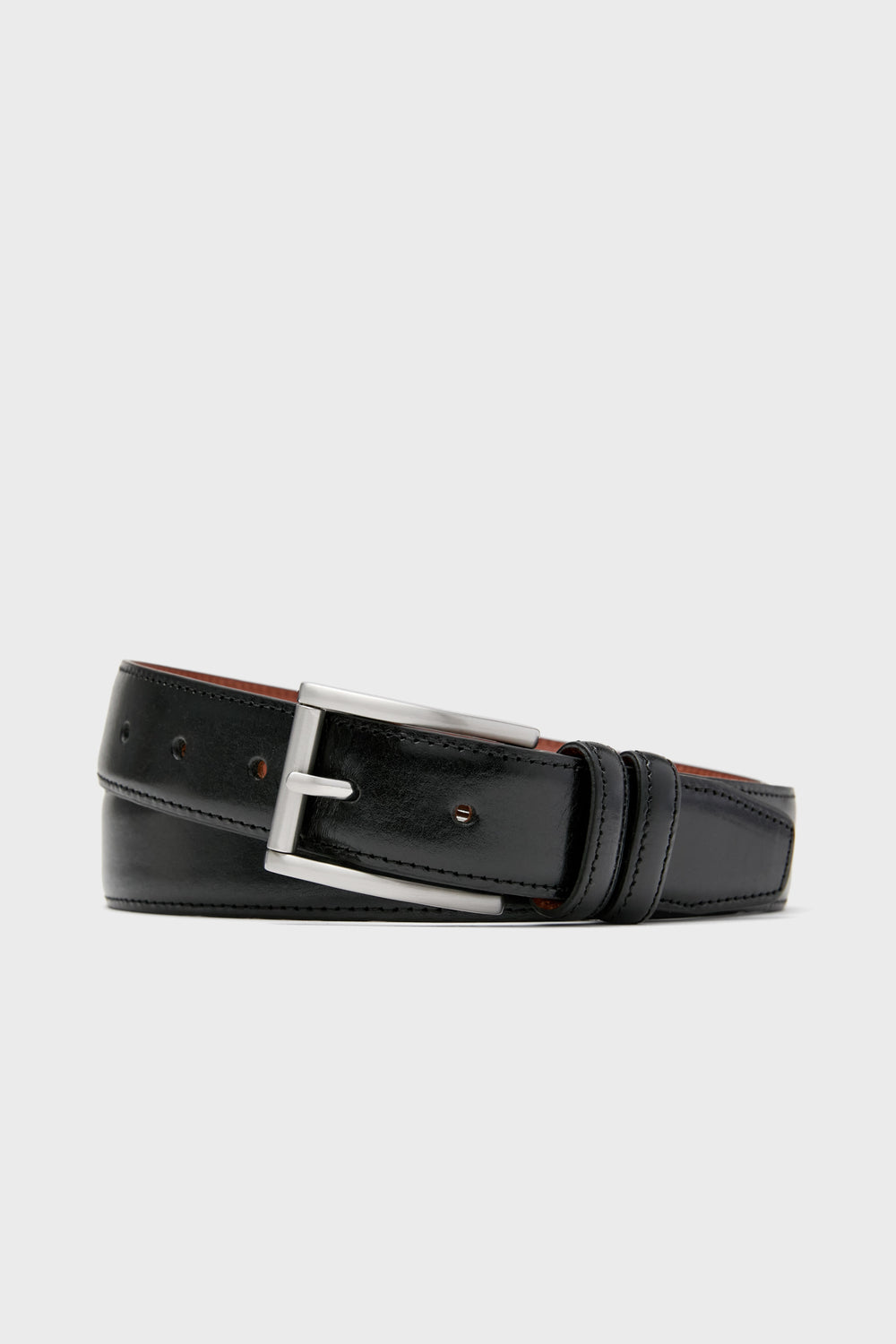 A black leather belt from Trafalgar, featuring a silver metal buckle, is coiled to showcase men's luxury accessories made from full grain leather.