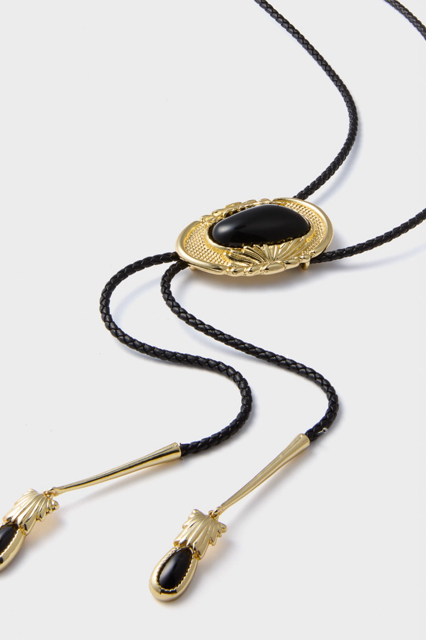 Gold and Black Dolly Bolo Tie Necklace: A classic, effortless accessory with a braided faux leather cord, gold-tone hardware, and striking black stone, adding fun, high-end flair to any outfit.
