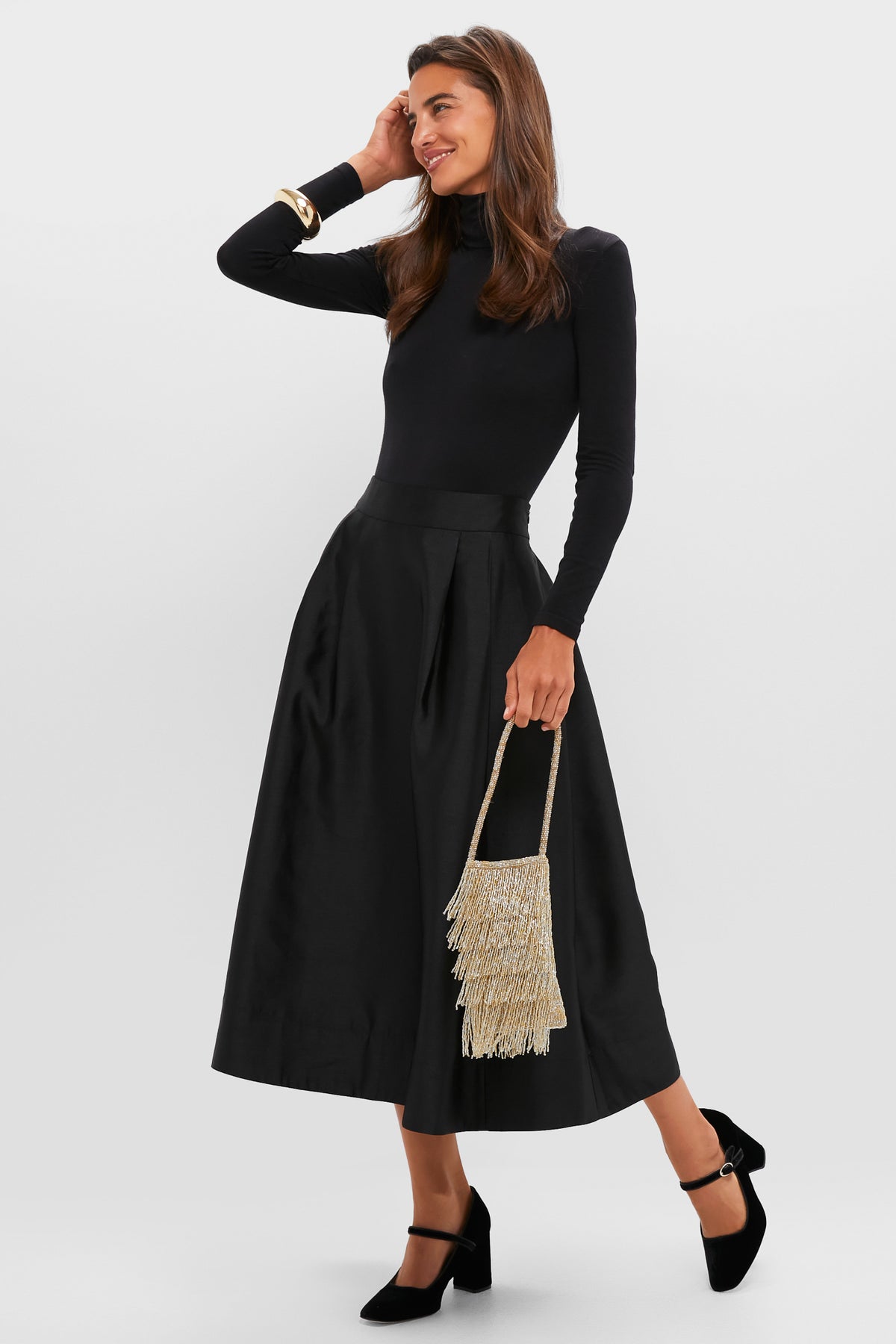 Woman in classic high-end fashion, showcasing Black Velvet Julia Heels with an effortless block heel, round toe, and gold buckle, paired with a chic gold evening bag.