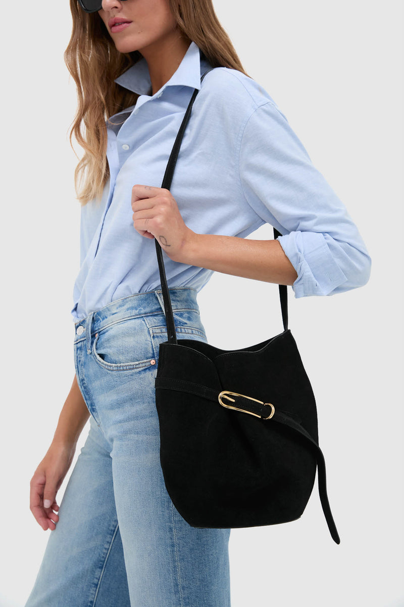 Person with classic Black Suede Belted Bucket Bag, featuring gold-tone buckle, effortlessly styled with light-blue shirt and jeans, embodying fun, high-end fashion.