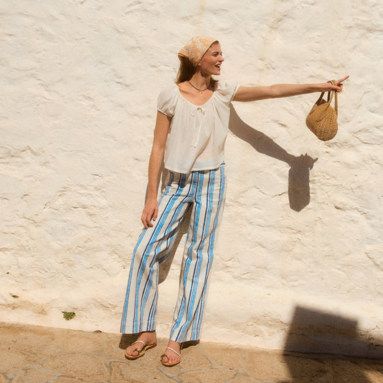 Woman standing in front of a wall in a white top and blue stripe pants 