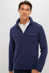 A man stands confidently in a Peter Millar sweater shirt jacket crafted from recycled performance fabric, layered over a white shirt.