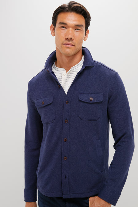 A man stands confidently in a Peter Millar sweater shirt jacket crafted from recycled performance fabric, layered over a white shirt.