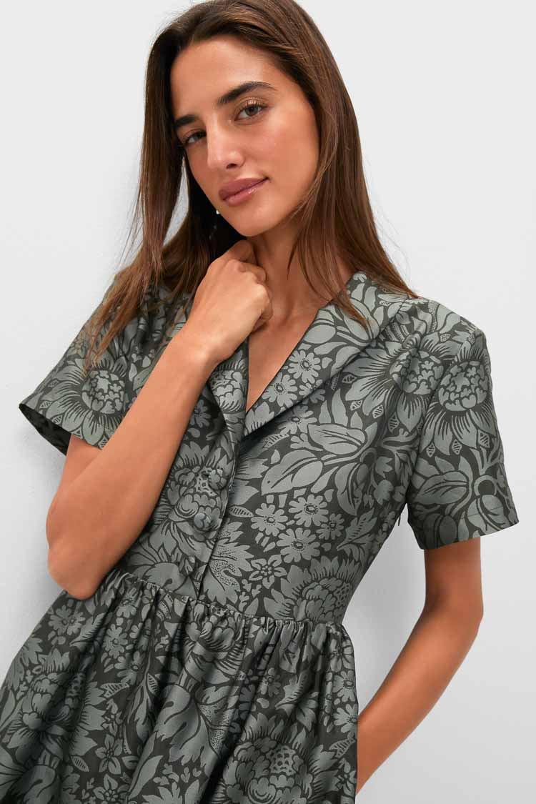 A woman wears a short-sleeved, collared V-neck Adelaide dress with a grey floral pattern from Tuckernuck, standing against a plain light background.