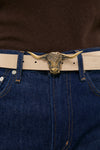 Brass Lansing Longhorn Buckle in polished brass, adorning a light-tan leather belt on dark denim jeans, offering a classic, effortless style with a high-end, fun twist.