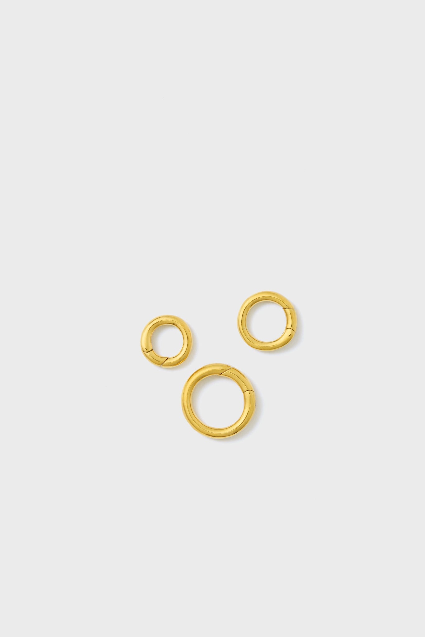 Three gold-tone brass hoop earrings of varying sizes from Tuckernuck Jewelry are displayed together.