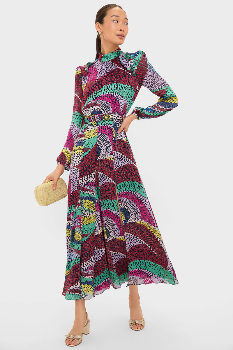 Model wearing the Jangle Jacqui-B Dress, a classic, high-end maxi with a colorful dot pattern, mock neck, and flowing skirt, styled with a woven clutch and sandals.