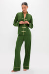 Woman models Douglas Fir Pima Cotton Wilford Women's Pajama Set, featuring a classic mandarin collar, effortless frog-style closures, and high-end yellow piping on forest-green fabric.